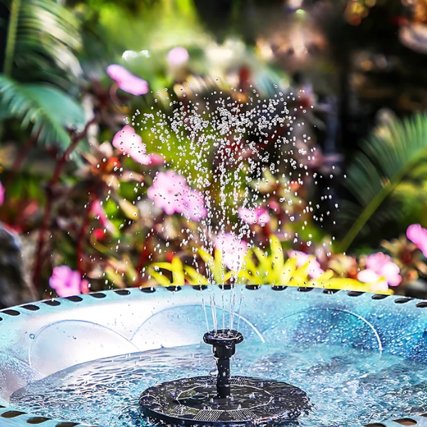Birdbath fountain spraying water into the air with colorful, blurred garden flowers in the background.